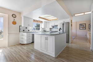 Kitchen with light wood finished floors, white cabinetry, decorative backsplash, appliances with stainless steel finishes, and a kitchen island
