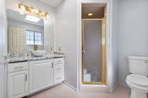 Primary Bathroom with vanity, a skylight, a shower stall, and light tile patterned floors