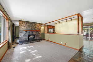 Unfurnished living room featuring a stone fireplace and track lighting