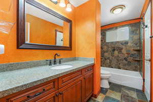 Full bathroom with vanity, bathing tub / shower combination, dark stone finish flooring, and a textured wall