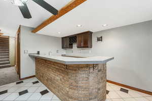 Indoor wet bar featuring dark brown cabinetry, light countertops, stairway, recessed lighting, and beam ceiling