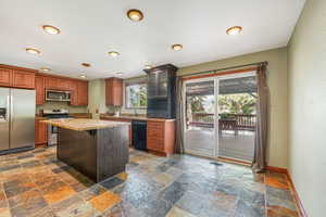 Kitchen featuring appliances with stainless steel finishes, a breakfast bar area, a kitchen island, stone tile floors, and brown cabinetry