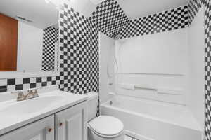 Full bath with tile walls, tub / shower combination, vanity, and backsplash