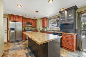 Kitchen featuring appliances with stainless steel finishes, glass insert cabinets, a center island, dark stone finish flooring, and recessed lighting
