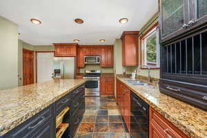 Kitchen featuring appliances with stainless steel finishes, light stone counters, brown cabinetry, dark cabinetry, and recessed lighting