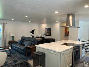 Kitchen with stainless steel appliances, island exhaust hood, open floor plan, light stone counters, and a kitchen island