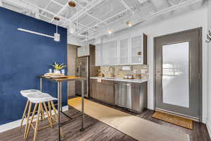 Bar area featuring white cabinets, backsplash, dark wood-type flooring, appliances with stainless steel finishes, and glass insert cabinets