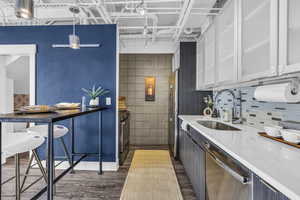 Kitchen with dark wood-type flooring, stainless steel appliances, white cabinets, tile walls, and a kitchen bar