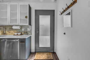 Kitchen with dishwasher, decorative backsplash, dark wood finished floors, light stone counters, and glass insert cabinets