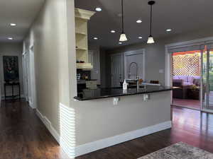Kitchen featuring dark wood-type flooring, recessed lighting, a peninsula, dark stone counters, and pendant lighting