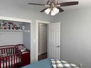Bedroom with a nursery area, ceiling fan, and dark wood-style floors