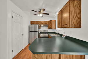 Kitchen with lofted ceiling, brown cabinets, stainless steel appliances, light wood-style floors, and ceiling fan