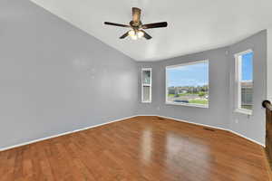 Empty room featuring wood finished floors, healthy amount of natural light, lofted ceiling, and ceiling fan