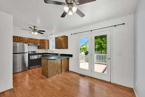Kitchen with brown cabinets, appliances with stainless steel finishes, dark countertops, light wood-type flooring, and a peninsula