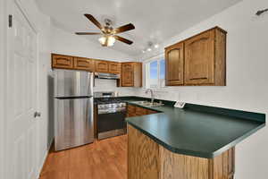 Kitchen featuring brown cabinets, a peninsula, appliances with stainless steel finishes, vaulted ceiling, and light wood-style flooring