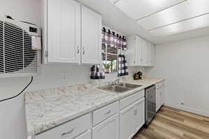 Kitchen featuring white cabinetry, light wood finished floors, light countertops, and a wall unit AC
