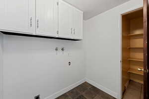 Laundry room with hookup for a washing machine, electric dryer hookup, dark tile patterned floors, and cabinet space