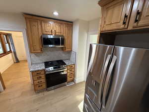Kitchen featuring stainless steel appliances, light stone countertops, decorative backsplash, light wood-style floors, and recessed lighting