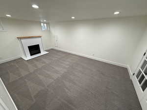 Below grade area with recessed lighting, a fireplace with raised hearth, and dark colored carpet. Could be primary bedroom or family room