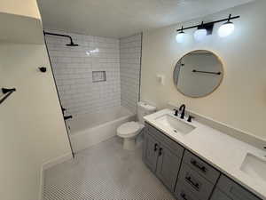 Full bath featuring double vanity, shower / bath combination, a textured ceiling, and light tile patterned flooring