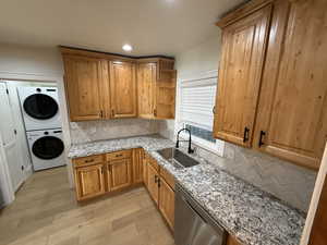 Kitchen with tasteful backsplash, open shelves, light stone counters, dishwasher, and estacked washer and dryer