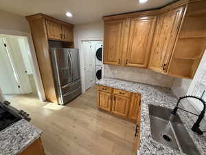Kitchen featuring light stone counters, stainless steel refrigerator with ice dispenser, open shelves, brown cabinets, and decorative backsplash