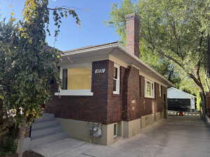 View of home's exterior with brick siding, an outdoor structure, a garage, and a chimney