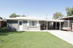 Back of house featuring a patio area, a carport, a yard, brick siding, and driveway