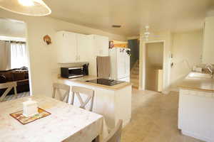 Kitchen featuring freestanding refrigerator, light countertops, a ceiling fan, stainless steel microwave, and white cabinetry