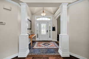 Entryway with ornate columns, dark wood finished floors, and vaulted ceiling