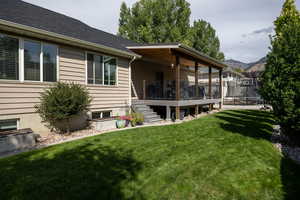 Rear view of house featuring a trampoline, a yard, a wooden deck, stairs, and a shingled roof