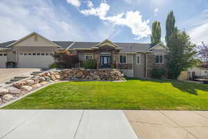 View of front of property featuring stone siding, roof with shingles, a garage, and a front lawn