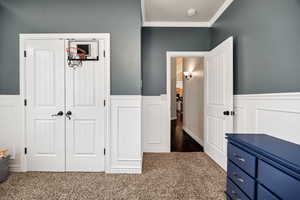 Bedroom 1 featuring crown molding, a wainscoted wall, dark carpet, a decorative wall, and a closet