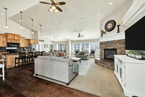 Living area featuring ceiling fan, a stone fireplace, dark wood-style floors, and high vaulted ceiling