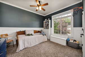 Bedroom 1 featuring ornamental molding, carpet flooring, a wainscoted wall, a ceiling fan, and a decorative wall