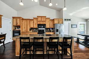 Kitchen featuring cabinetry, pendant lighting, tasteful backsplash, black appliances, and a kitchen island with sink