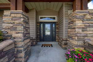 Doorway to property with stone siding and covered porch
