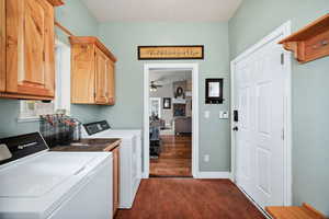 Laundry area with a stone fireplace, cabinet space, ceiling fan, dark wood-style flooring, and washing machine and dryer