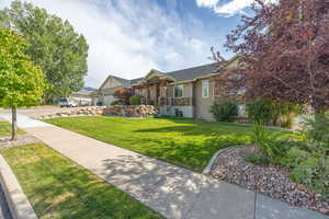 View of front facade featuring a front yard, stone siding, and an attached garage