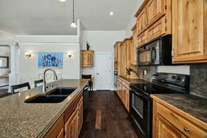 Kitchen featuring black appliances, dark wood-type flooring, tasteful backsplash, a kitchen breakfast bar, and decorative columns