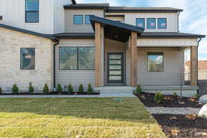 Entrance to property with board and batten siding, stone siding, a yard, and a porch