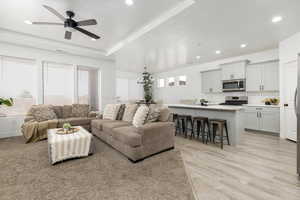Living room with a tray ceiling, a ceiling fan, recessed lighting, and light wood-style floors