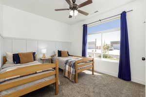 Carpeted bedroom featuring a decorative wall and a ceiling fan