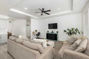 Living room featuring a raised ceiling, ceiling fan, and recessed lighting