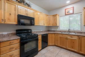 Kitchen with black appliances, light tile patterned flooring, dark countertops, and light brown cabinetry