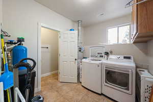 Laundry area featuring light tile patterned floors, cabinet space, washing machine and clothes dryer, and strapped water heater