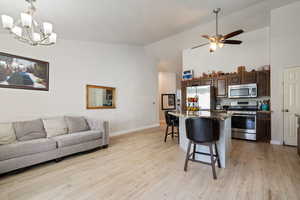 Kitchen featuring appliances with stainless steel finishes, open floor plan, a kitchen breakfast bar, dark brown cabinets, and high vaulted ceiling