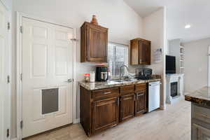 Kitchen with light wood-type flooring, stainless steel dishwasher, dark brown cabinetry, a glass covered fireplace, and recessed lighting