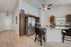 Kitchen featuring a kitchen bar, appliances with stainless steel finishes, a kitchen island, light wood-style floors, and high vaulted ceiling