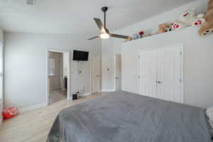 Bedroom with lofted ceiling, light wood-style flooring, a ceiling fan, and ensuite bathroom